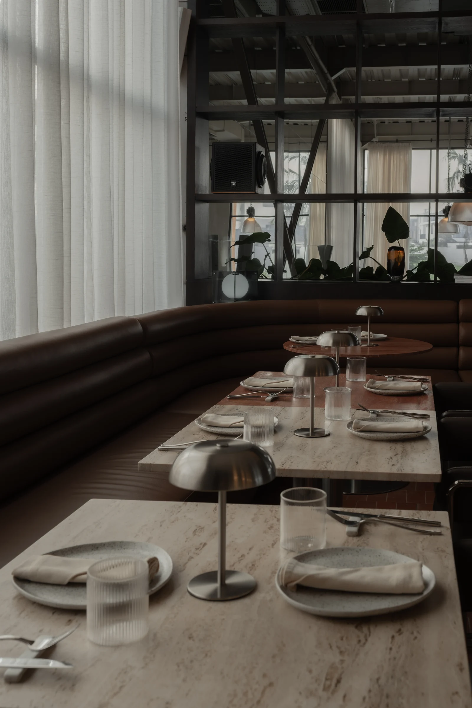A dining table beside sheer curtains and a warm leather banquette.