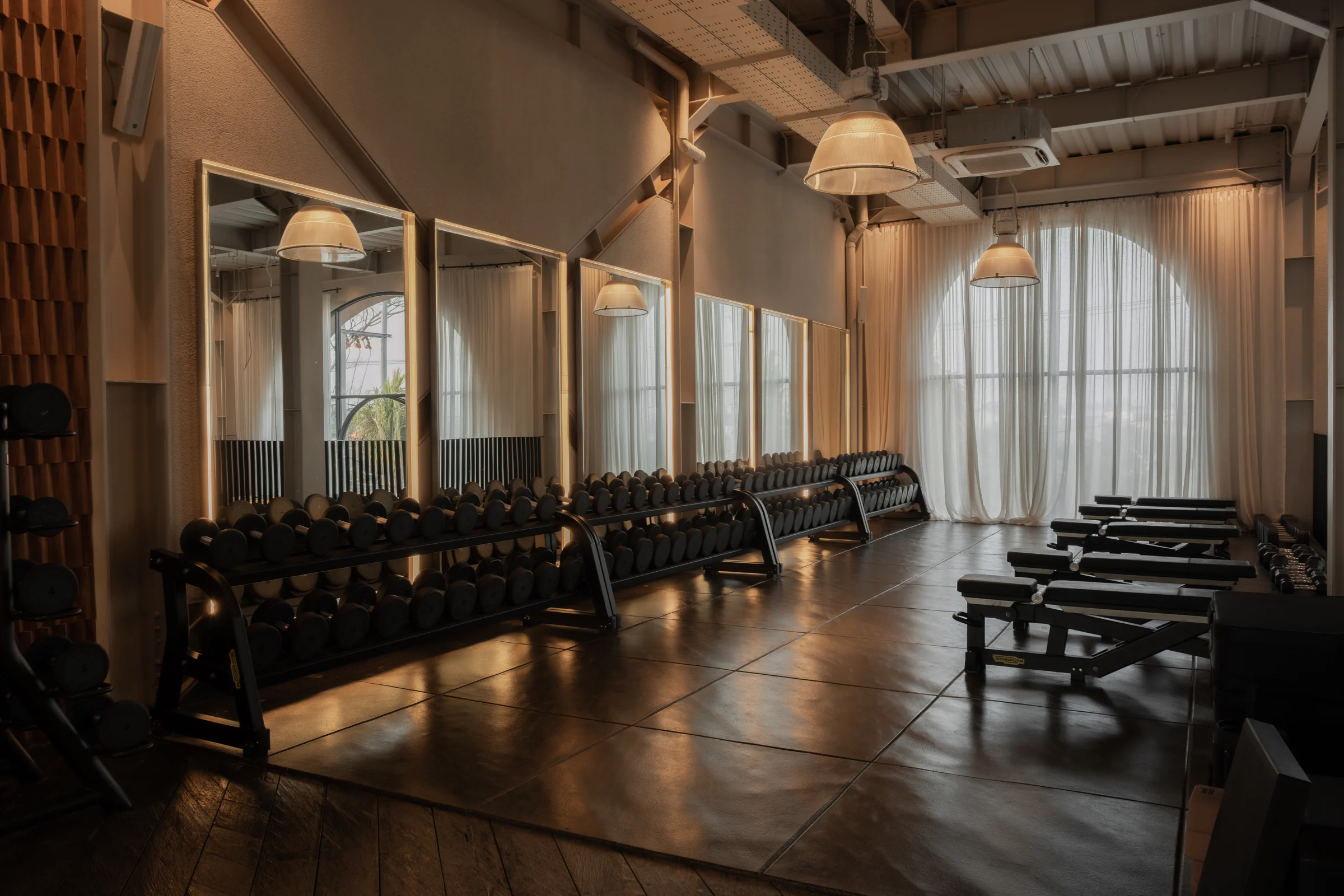 Dumbbell racks and adjustable benches along the mirrored free-weight area.