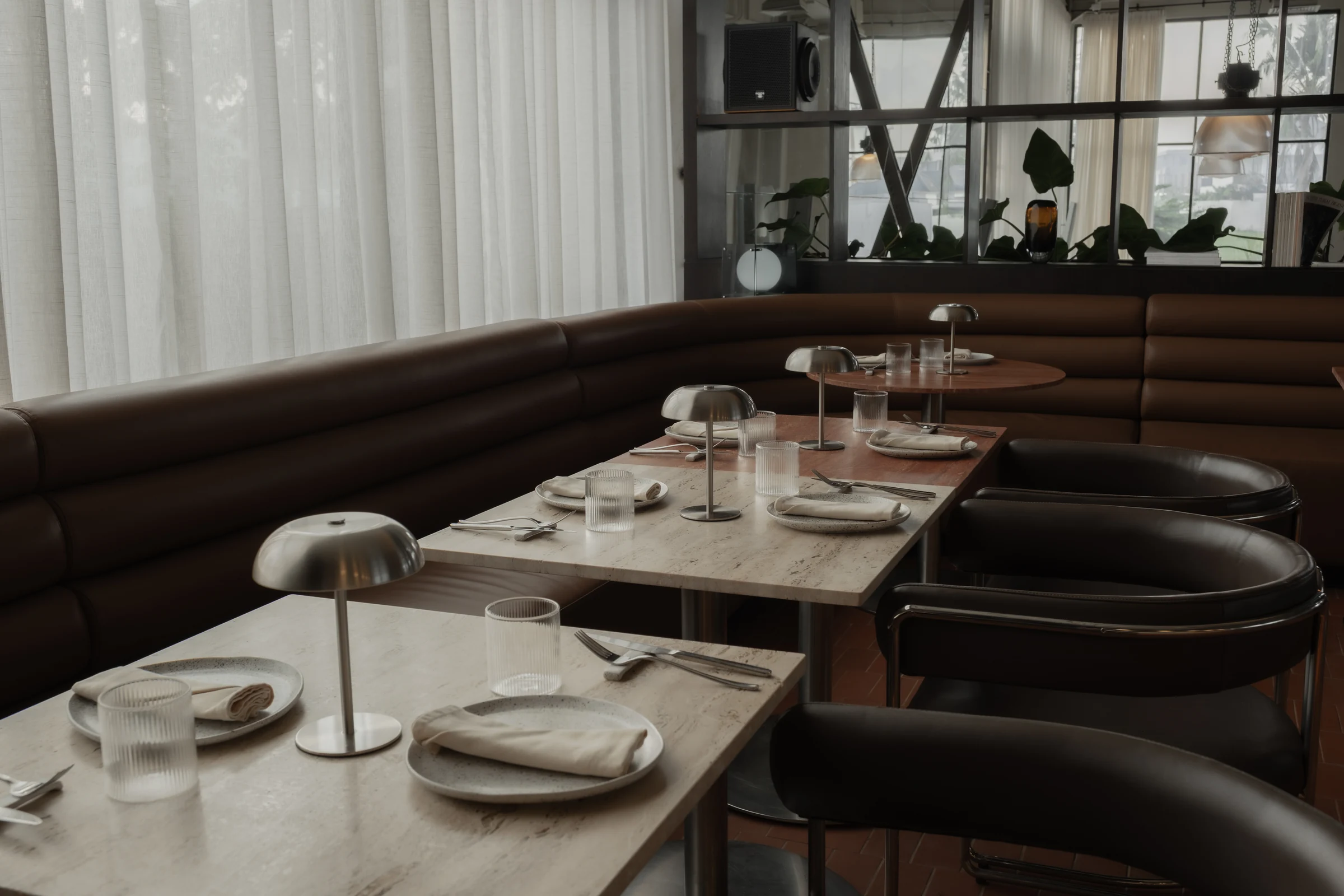 Marble dining tables set with glasses and plates beside a curved leather banquette.