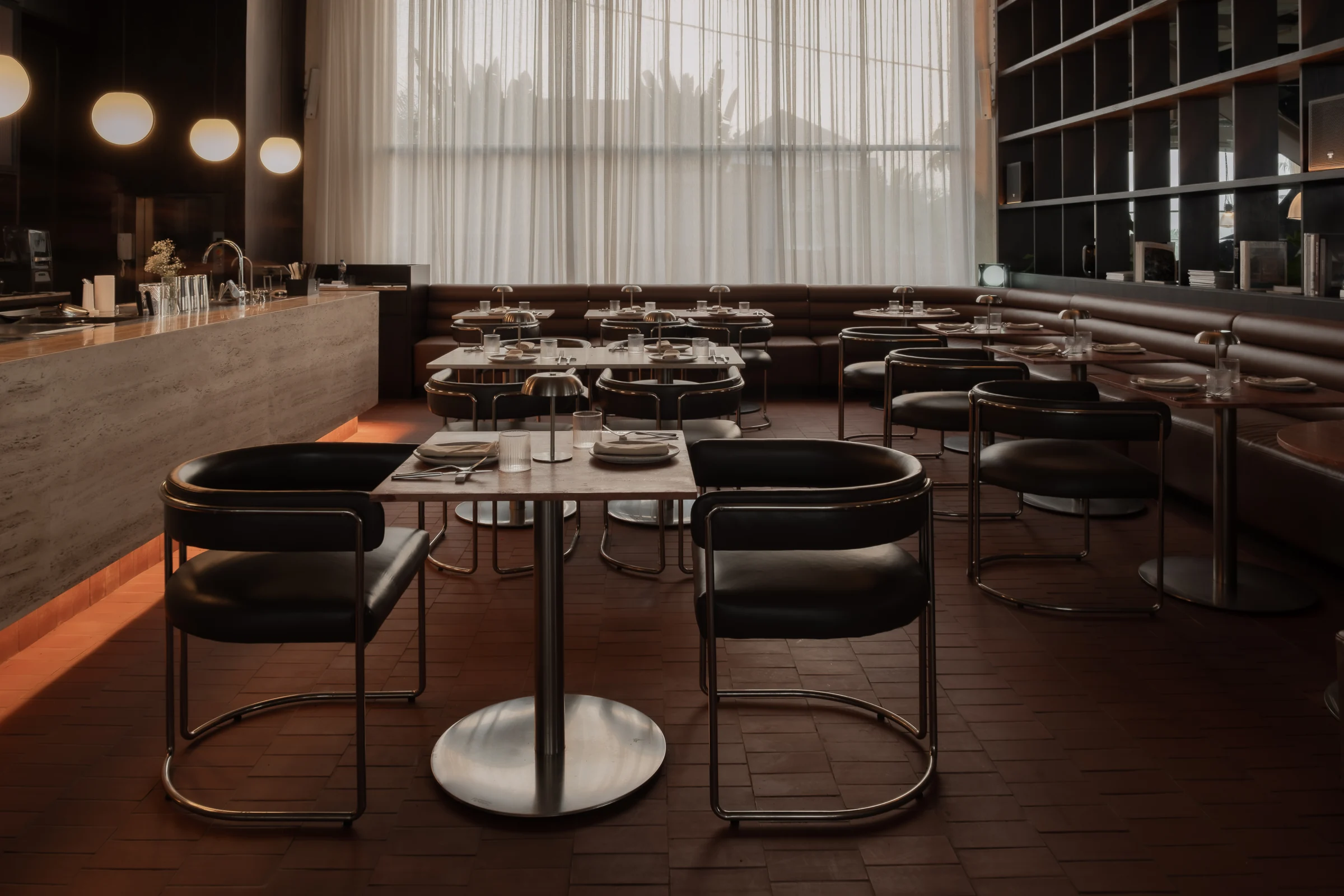 Rows of dining tables and leather chairs beside tall windows and timber shelving.