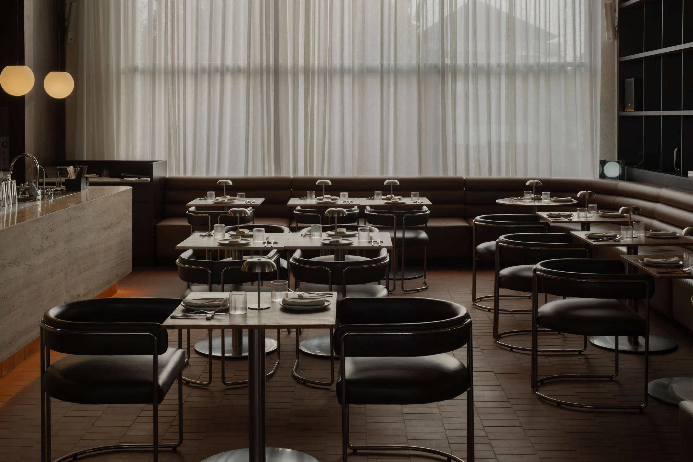 Curved leather chairs and tables set for dining beside sheer curtains.