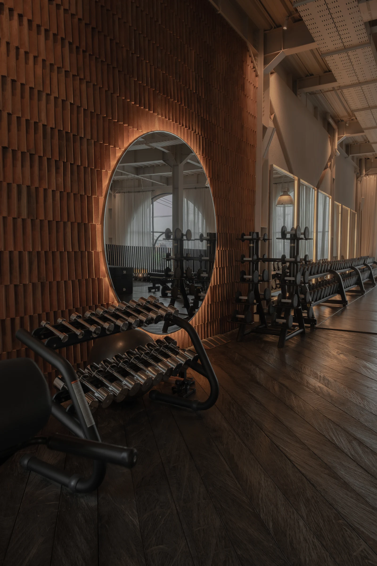 An illuminated circular mirror on a textured brick wall beside a row of dumbbells.