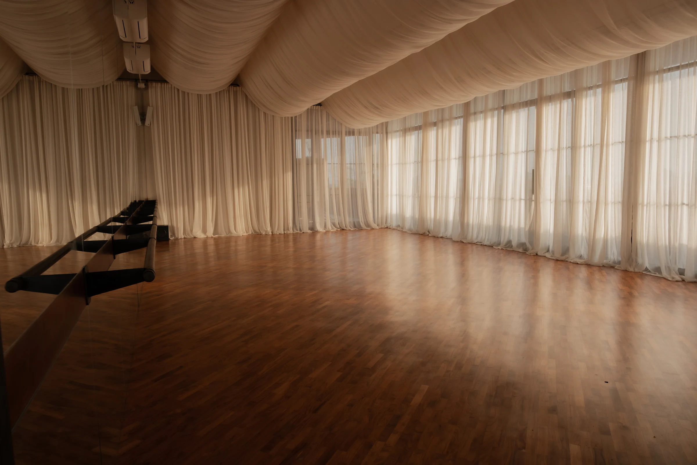 An open timber-floored studio with full-height mirrors, sheer curtains and a softly draped ceiling.