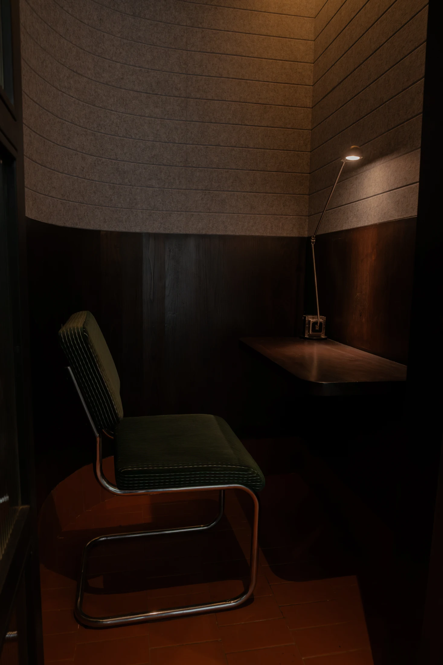 A green upholstered chair, timber desk and task light inside a softly lit call booth with acoustic wall panels.
