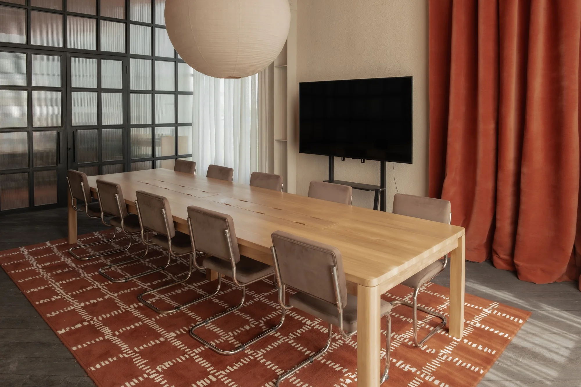 A long timber table and leather chairs beneath a paper pendant in the library room.