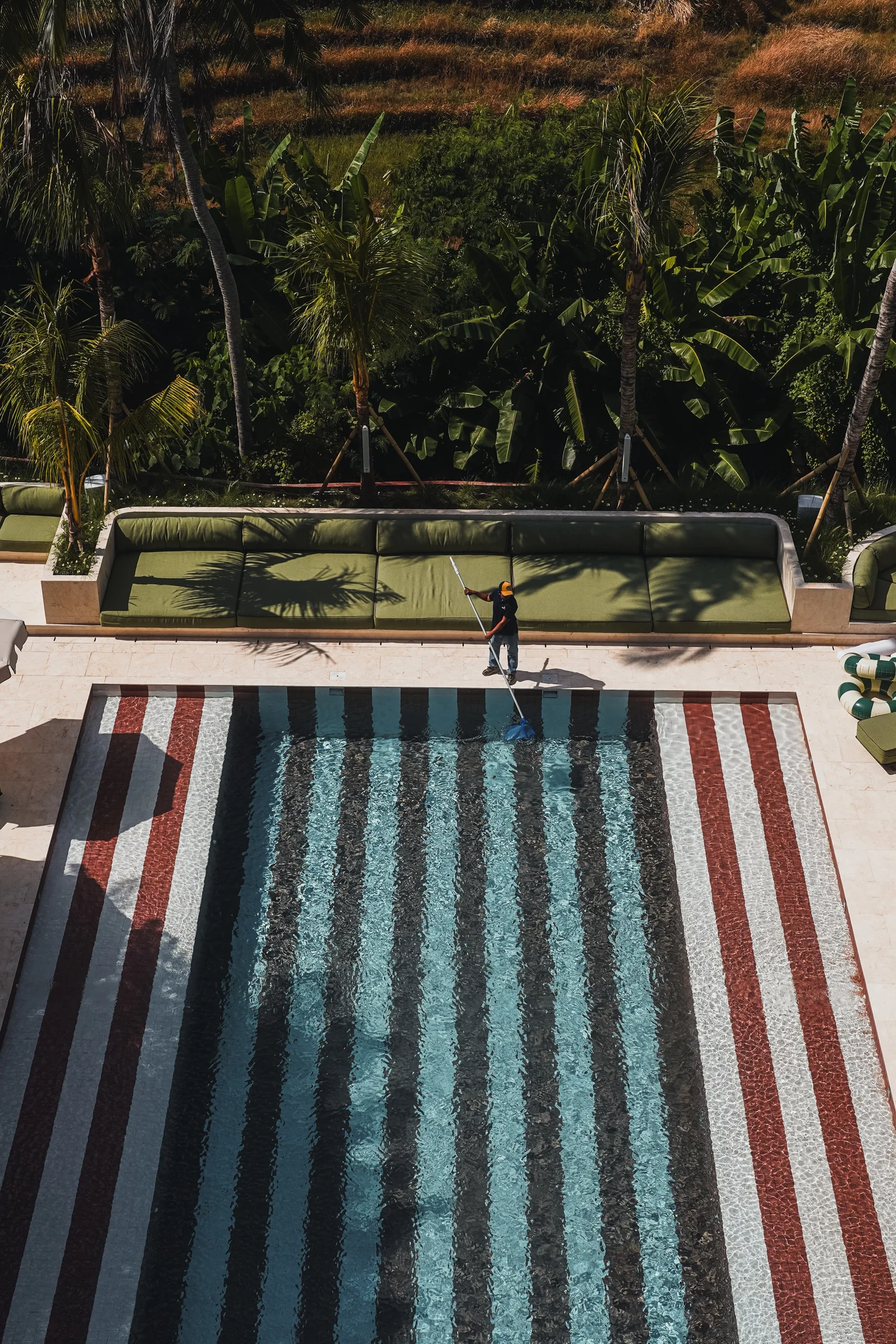 The striped swimming pool beside green loungers and a lush tropical garden.
