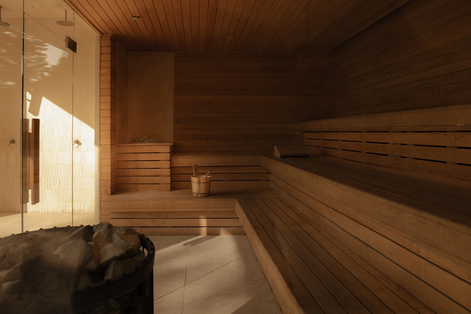 Sunlight falling across timber benches and a stone heater inside the sauna.