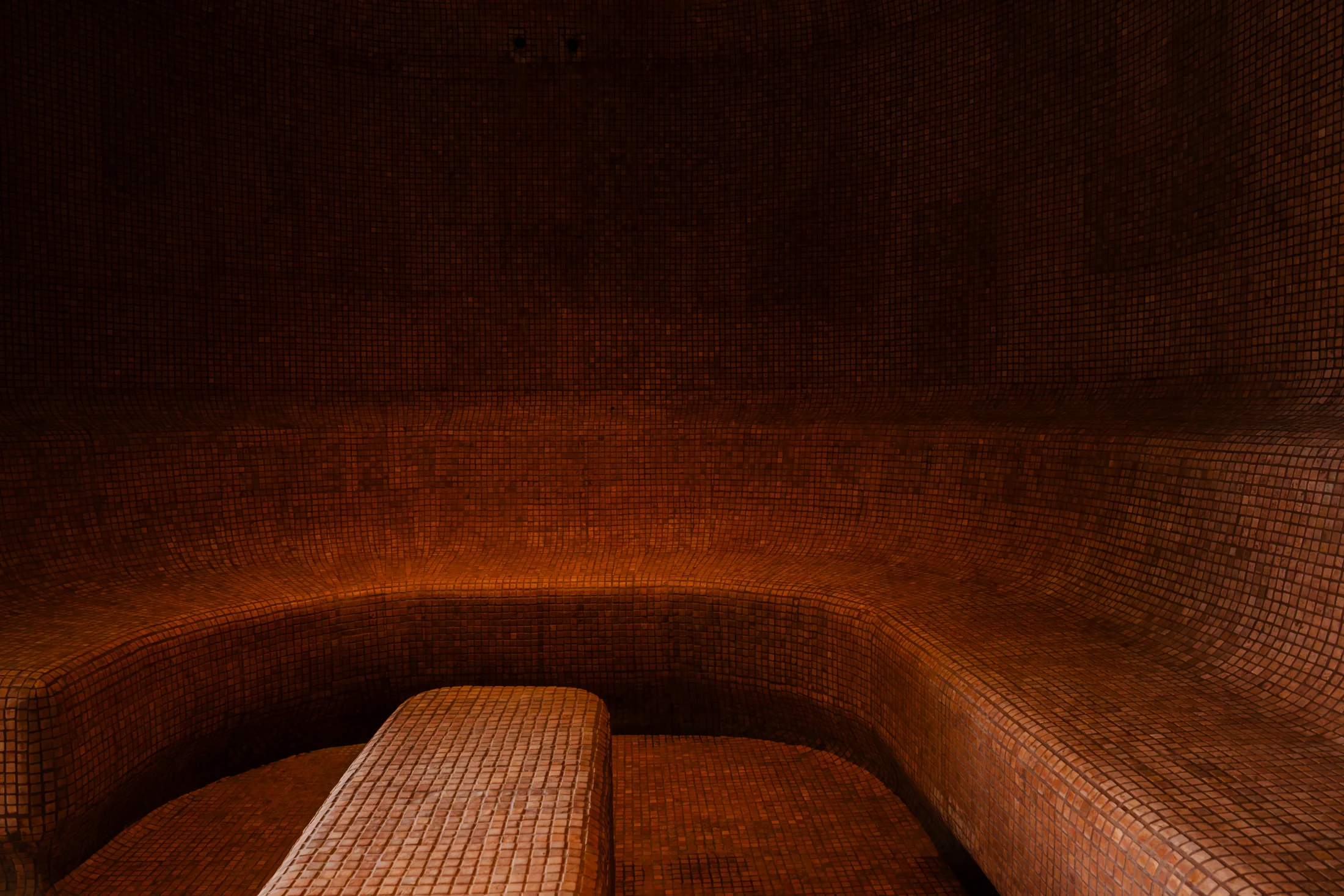 Curved benches and a central seat covered in warm terracotta mosaic tiles inside the steam room.