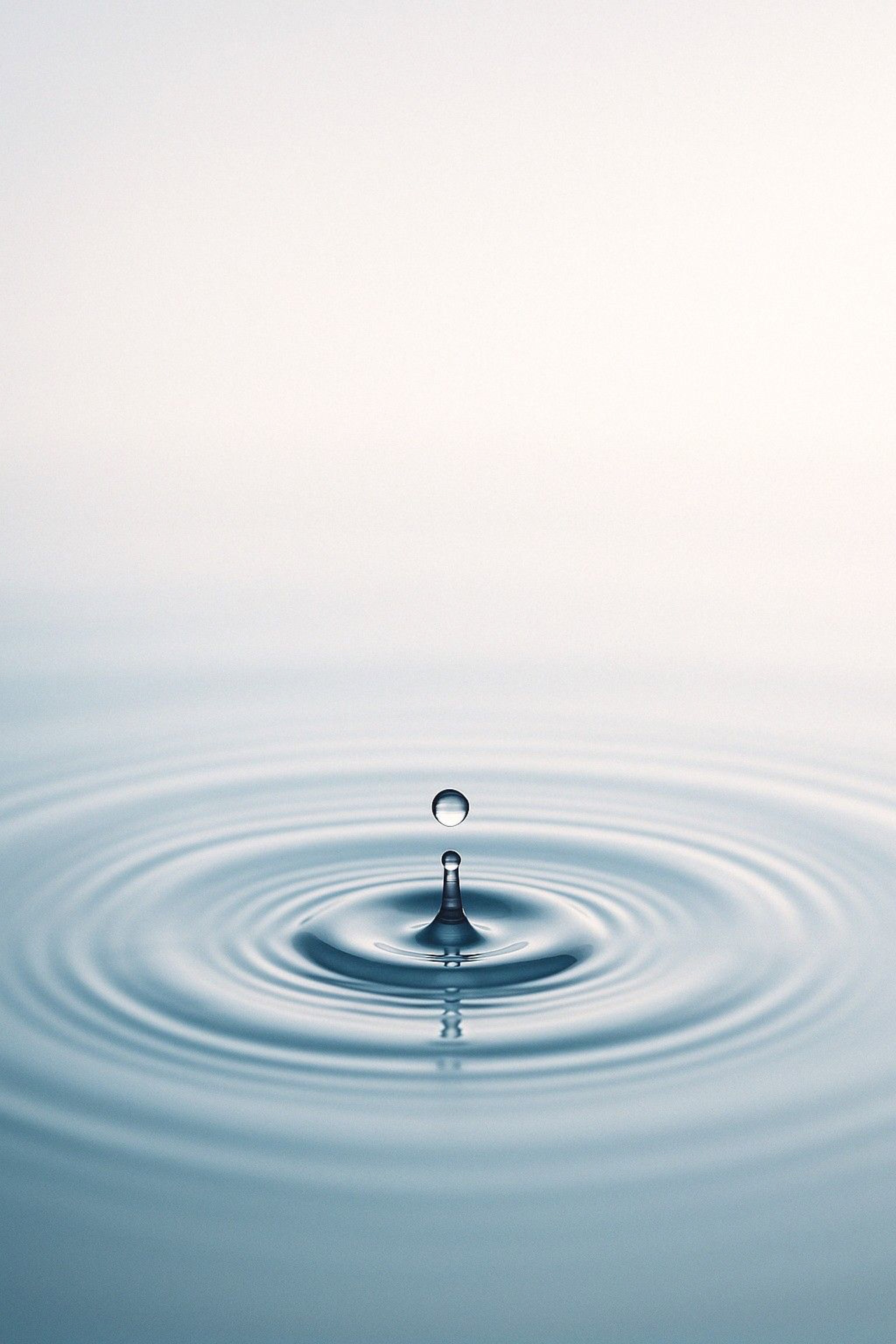 A clear droplet falling into still water, creating gentle ripples.